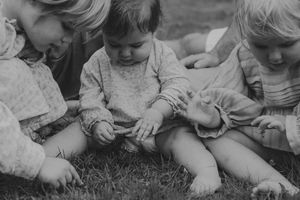 Black and white photo of three young siblings sitting together on grass, examining something.