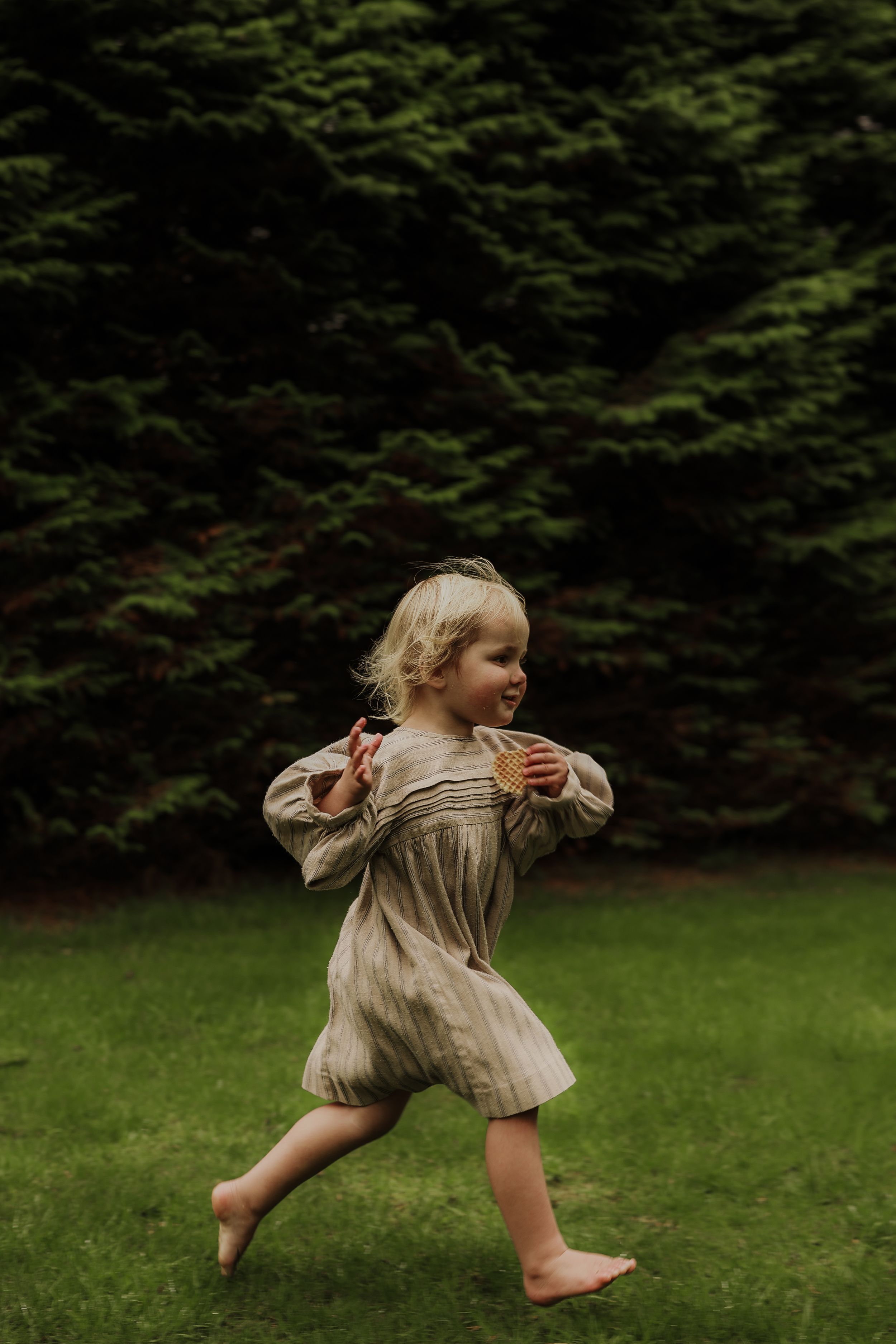 Barefoot young girl in linen dress running joyfully on green grass.