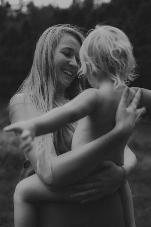 Black and white photo of a smiling mother hugging a young child outdoors in nature.