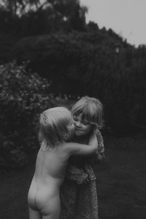 Two young siblings sharing a tender hug outdoors in black and white.