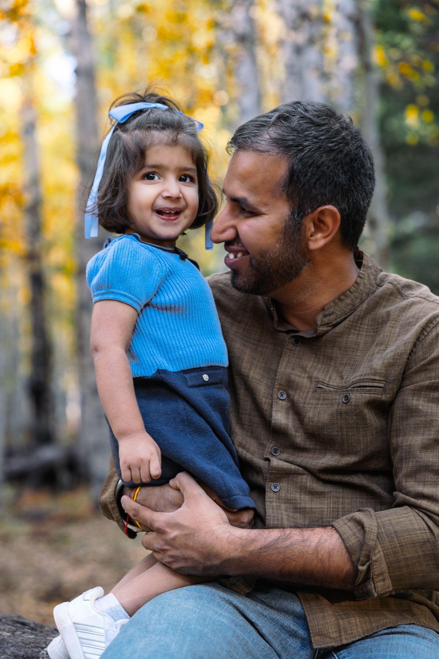 A parent and child share joyful moments together in an autumn forest setting with golden foliage in the background.
