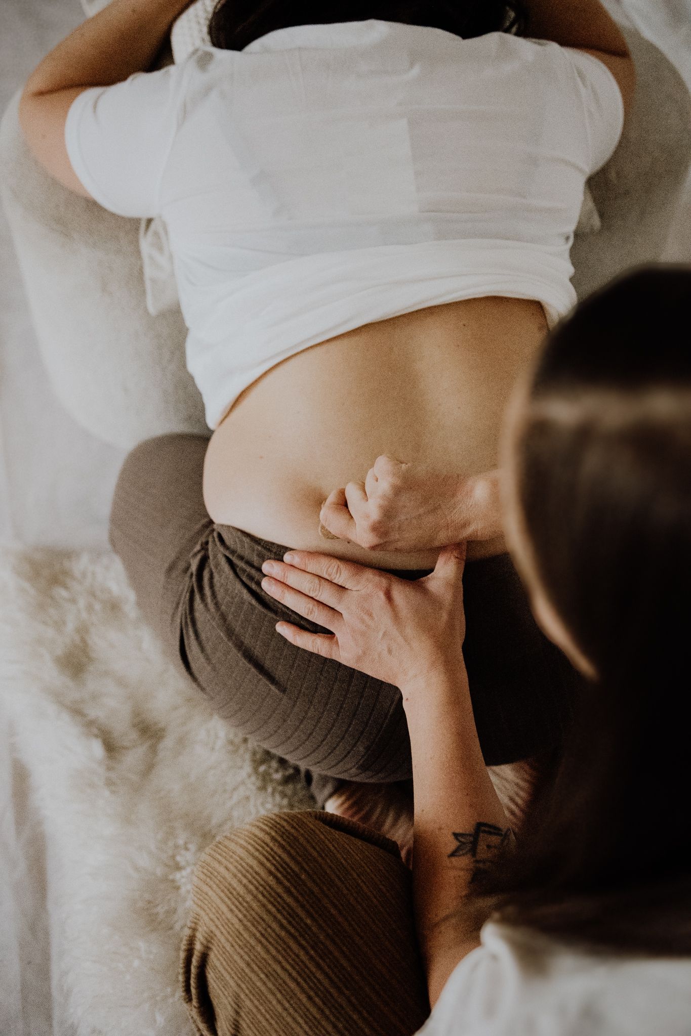 Intimate maternity photography series showing pregnant woman's belly in white shirt against brown fabric backdrop.