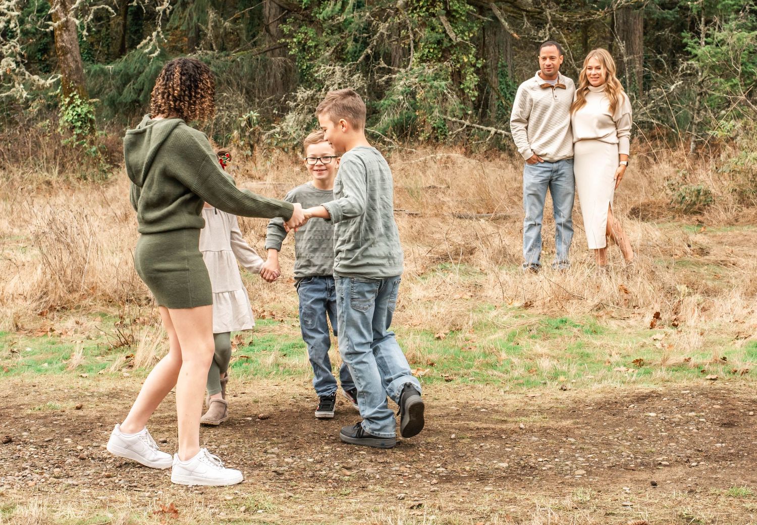 People gather in a rustic outdoor setting with brown grass and trees in the background.