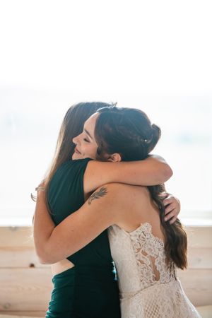 A tender embrace between two people in a sunlit outdoor setting, one wearing a white lace gown.