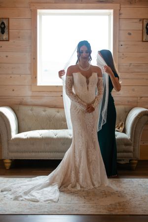 A wedding dress fitting scene shows two women in a rustic room with wooden walls and a tufted couch.