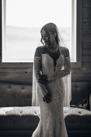 Black and white portraits of a bride in a long-sleeved lace dress standing by a window.