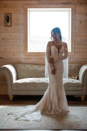 Full-length view of a lace wedding gown with train against bright window in rustic room.