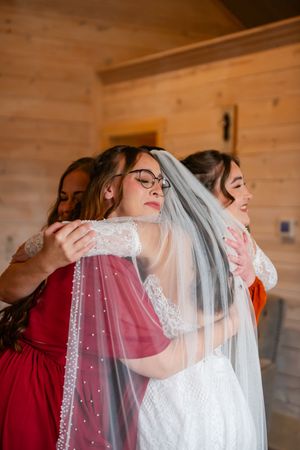 Emotional wedding preparation moment with attendants helping adjust the bride's pearl-studded veil.