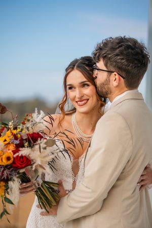 Romantic autumn wedding couple embraces outdoors with vibrant fall bouquet featuring sunflowers and roses.