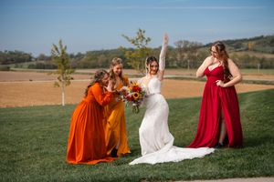 Wedding party in burgundy and orange dresses posing together in a sunny outdoor field.