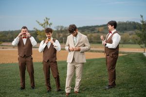 Groomsmen in brown vests and beige suit share a lighthearted moment outdoors.