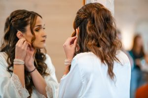 A stylist works on a client's wavy brown hair in a bright salon setting.