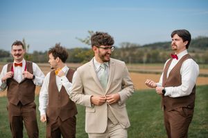 Groomsmen in brown vests and khaki suits sharing laughs outdoors on wedding day.