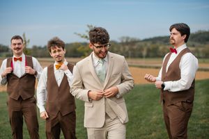 Groomsmen in brown vests and tan suits pose together outdoors on a sunny day.