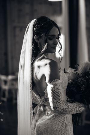 Dramatic black and white portrait of bride in lace gown with flowing veil.