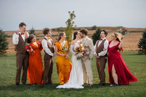 Wedding party in burgundy and orange dresses poses together on grassy field.