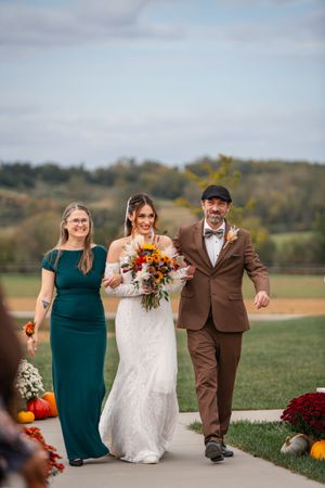 Wedding party walks and laughs together on grassy hill wearing brown and teal attire.