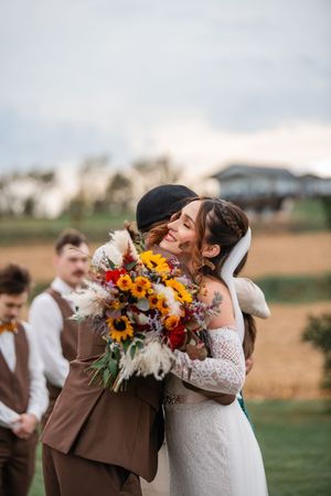 Newlyweds share first kiss while holding vibrant sunflower bouquets outdoors.