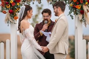 Autumn wedding ceremony under floral arch with orange and red blooms.
