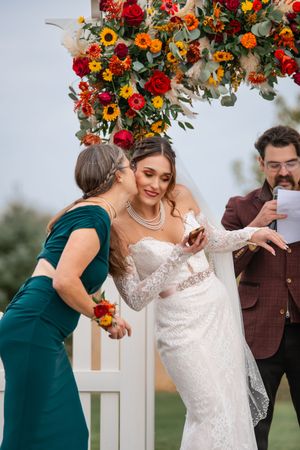 Wedding ceremony under a floral arch with vibrant red and orange flowers and sunflowers.