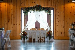 A rustic wooden barn interior decorated for a wedding reception with white tables and chairs under warm lighting.