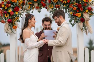 Wedding ceremony under arch decorated with vibrant autumn flowers and greenery.