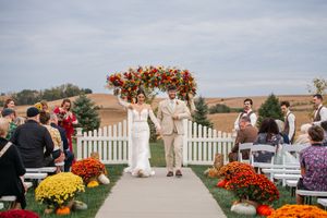 Outdoor wedding ceremony setup with white picket fence and colorful fall floral arrangements.