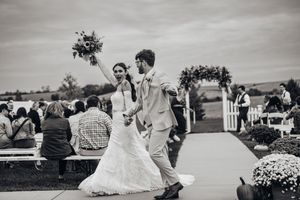 A black and white panoramic view of an outdoor wedding ceremony with guests seated on a rolling hillside.