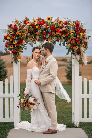 Romantic wedding moments captured under a colorful floral arch with white picket fence backdrop.
