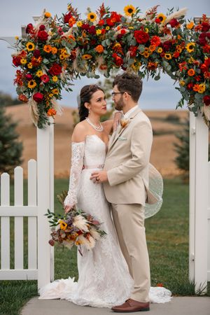 A romantic wedding scene under an arch decorated with vibrant sunflowers and red roses.