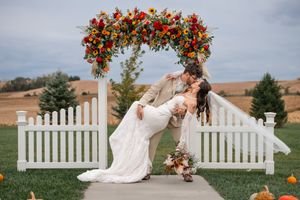 Wedding ceremony setup with vibrant red and orange floral arrangements on white picket fence.