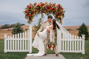 Rustic outdoor wedding ceremony with white picket fence and fall floral arrangements.