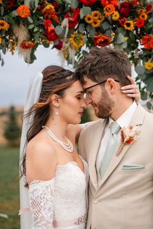 Intimate wedding portraits under a floral arch with sunflowers and autumn blooms.
