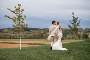 Romantic wedding couple poses across scenic countryside landscape.