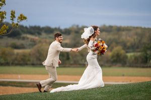 Newlyweds share playful moments on grassy hill during autumn wedding photoshoot.