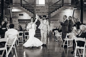 Wedding reception in rustic barn venue with wooden beams and white chairs.