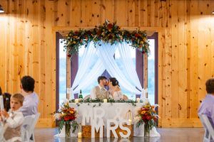 Rustic wooden barn wedding reception space decorated with floral arrangements and white drapery.