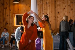 Wedding reception guests dancing and celebrating in rustic wooden barn venue with warm lighting.