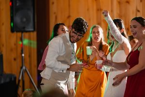 Wedding guests dancing and celebrating at a lively barn reception with wood paneled walls.