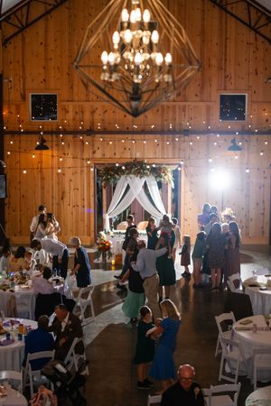 Elegant barn wedding reception setup with chandeliers, white draping, and round tables.
