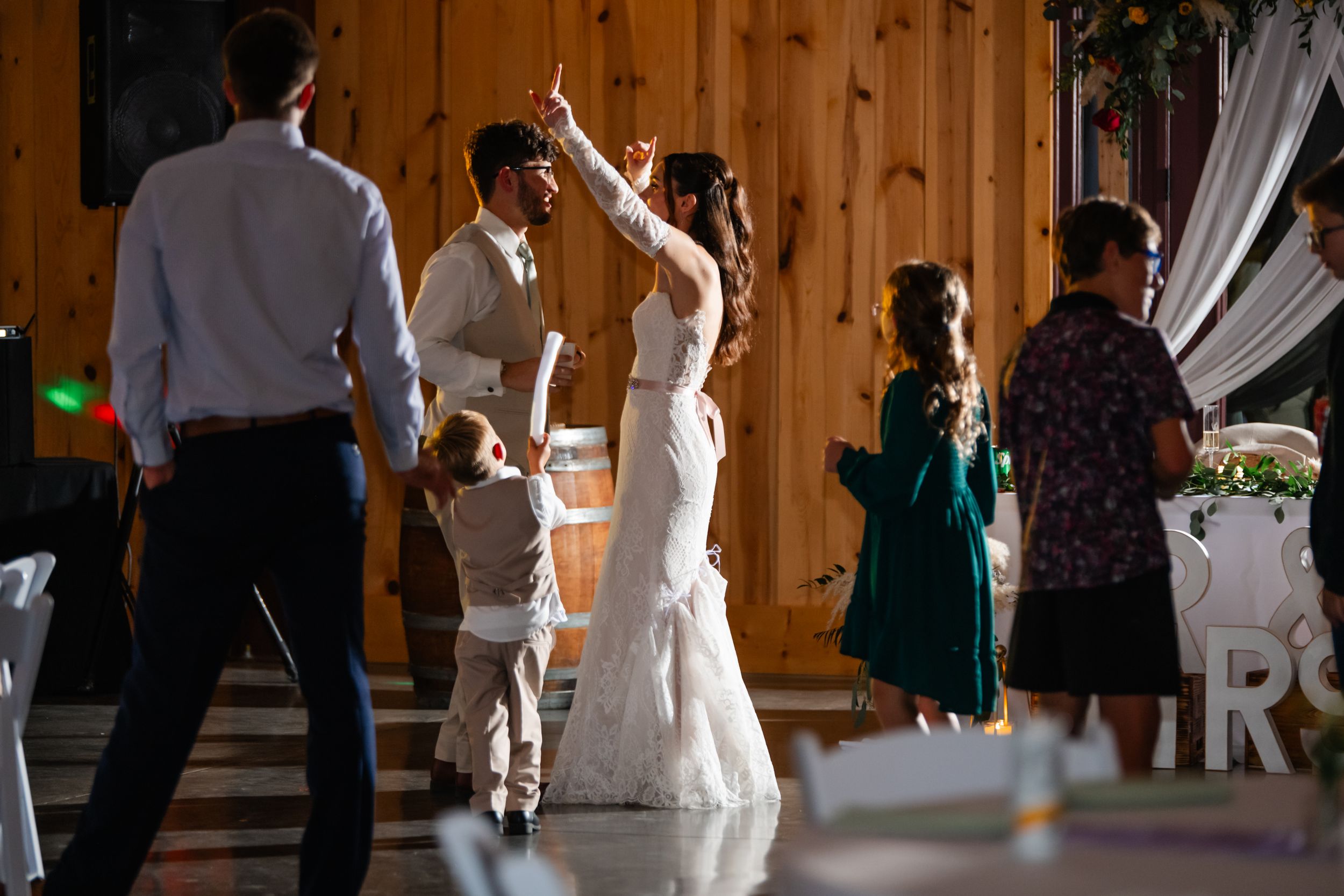 Wedding party dancing and celebrating in rustic wooden venue with ambient lighting.