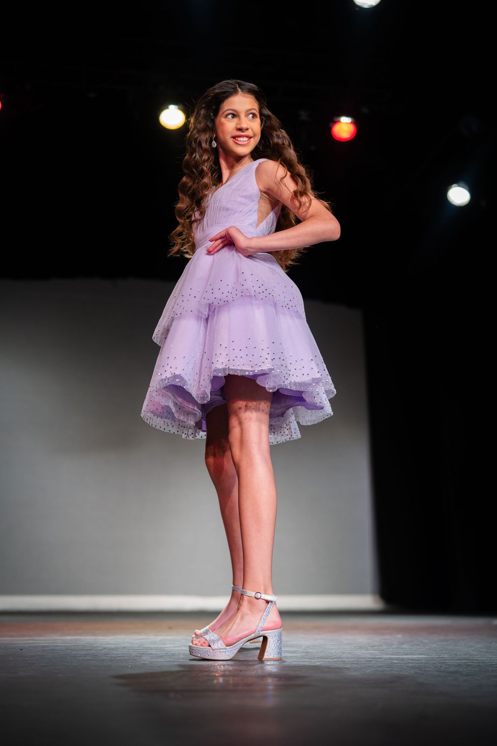 Dancer in flowing lavender dress performing gracefully on dark stage.