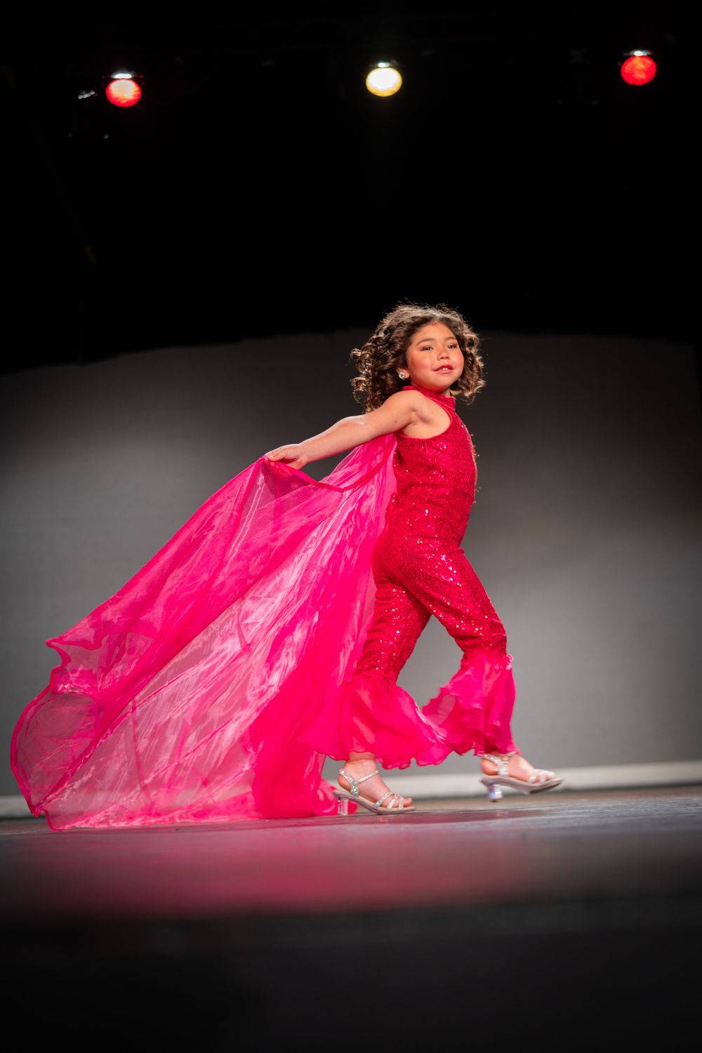 Dancer in flowing red gown performing dramatic floor choreography under stage lights.