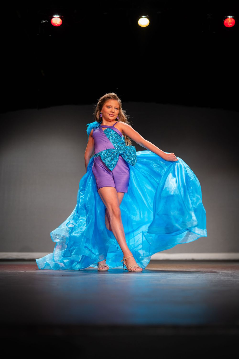 Dancer in purple outfit with flowing blue cape performing on stage.
