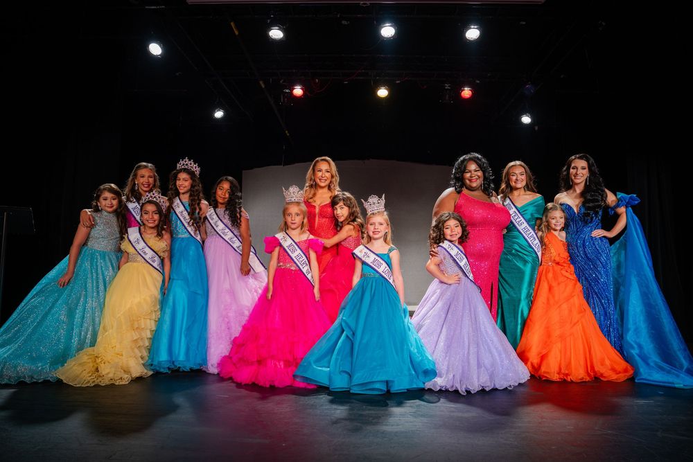 Colorful pageant gowns shine on stage during a performance in a dark theater setting.