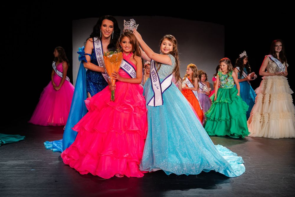 Colorful pageant gowns in bright pink, blue and green sparkle under stage lights during a performance.
