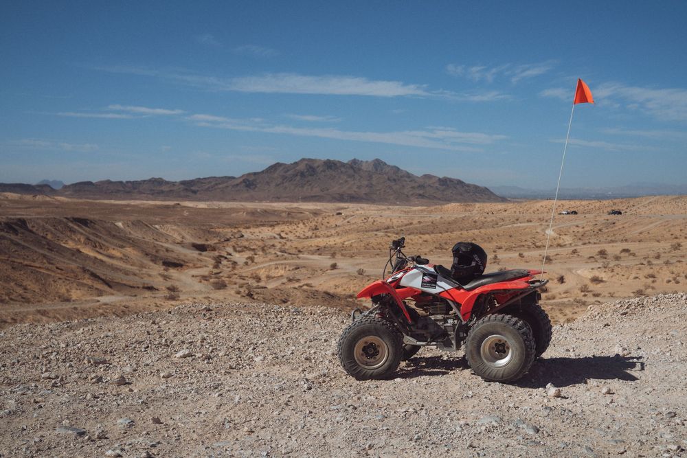 ATV and motorcycle parked on desert gravel with rugged mountains in the background.