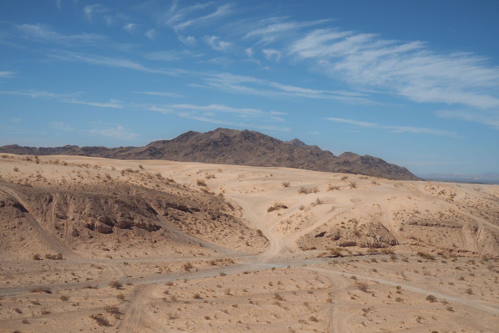 Panoramic view of barren desert landscape with distant mountains under scattered clouds.