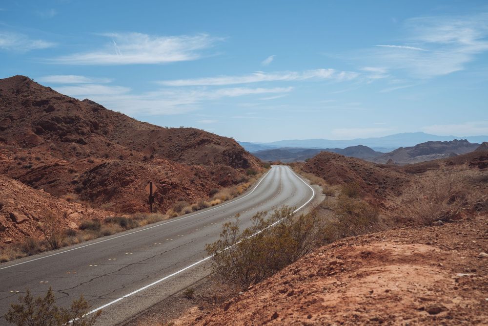 Curved desert highway winds through red rock formations under bright blue sky.