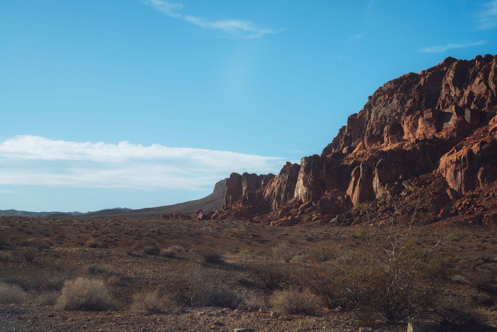 Rugged desert landscape with towering red rock cliffs and sparse vegetation under clear blue skies.